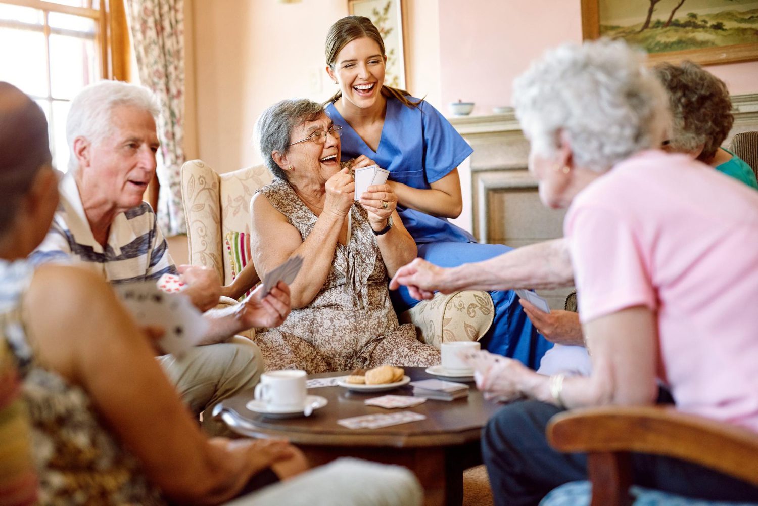 Care home residents enjoying cards and tea with smiling carer